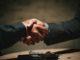 two people shaking hands over a wooden table